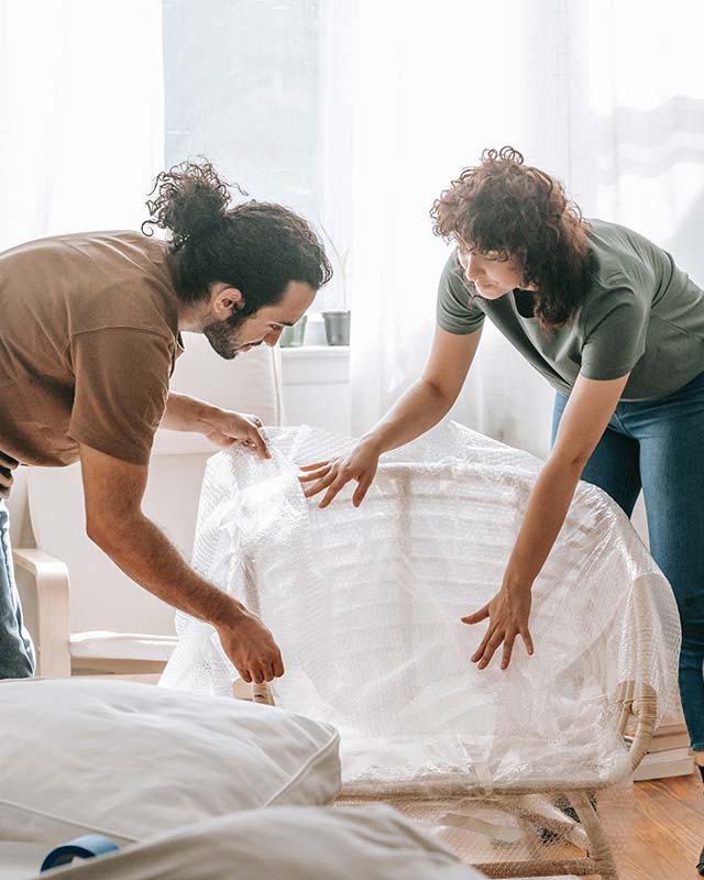 Två personer packar en möbel med bubbelplast