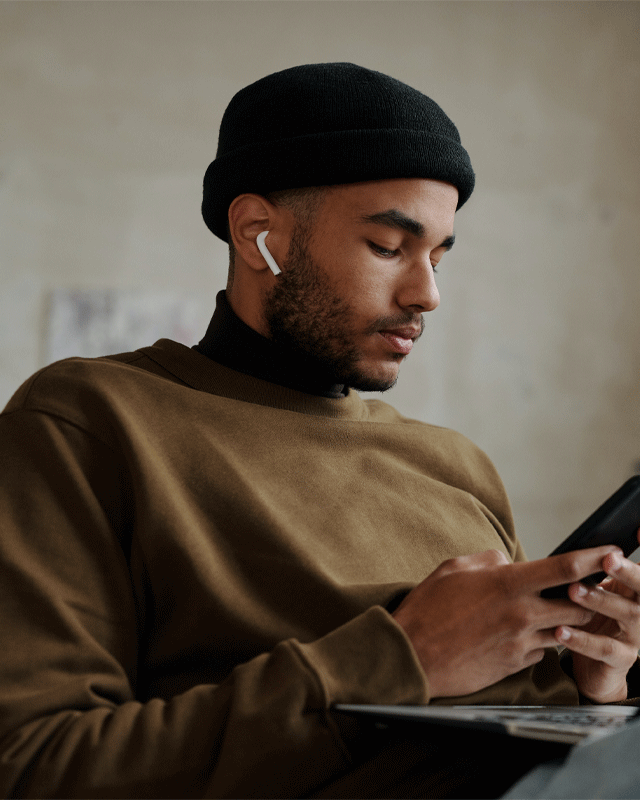 En kille med hörlurar tittar på sin telefon